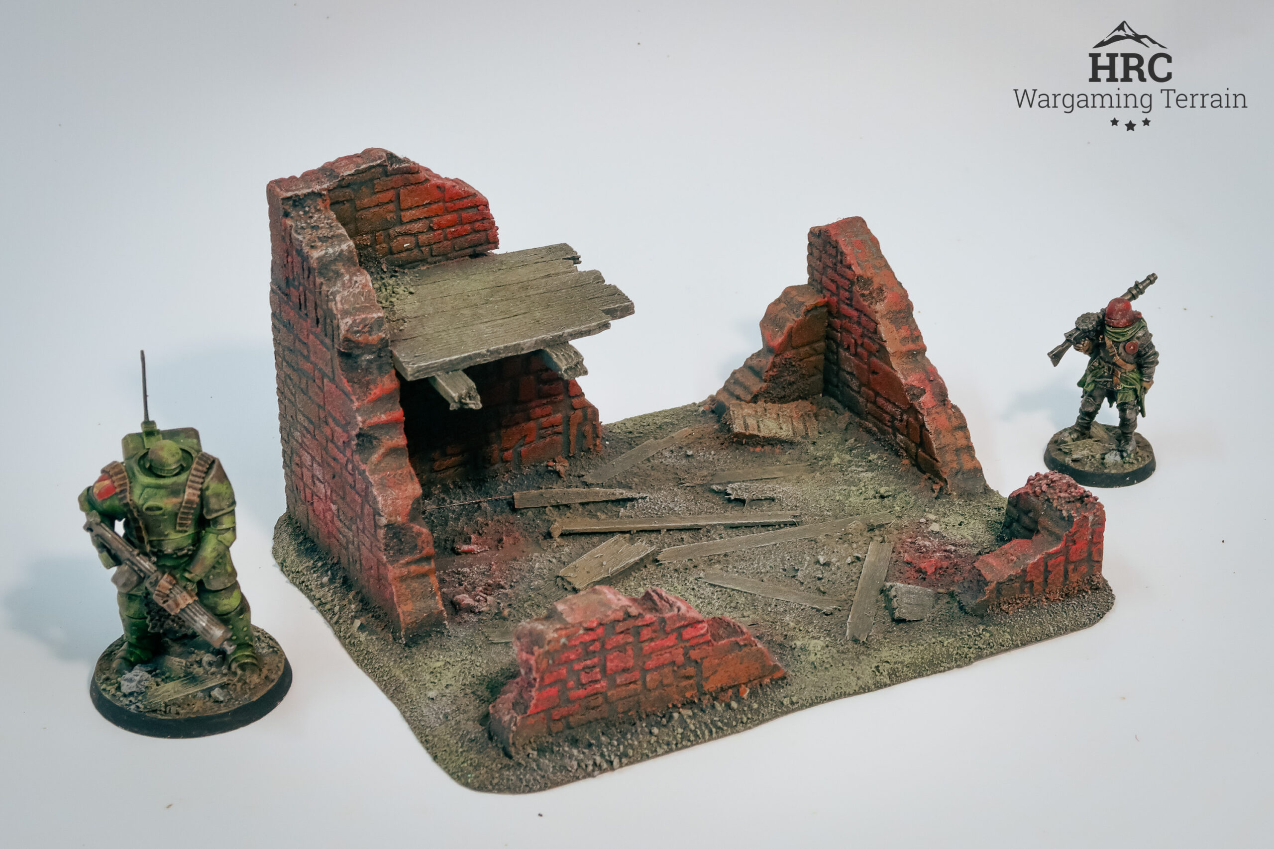 Detailed charred beams and rubble on a ruined brick shelter, hand-painted wargaming scenery.